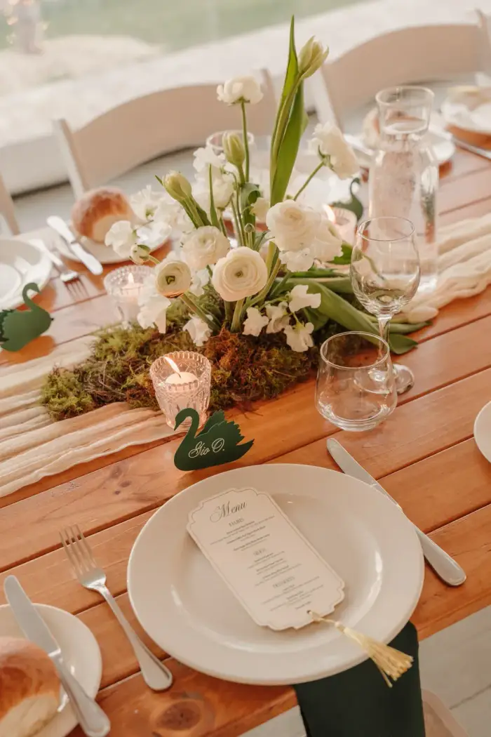 Place setting with a low white and green centrepiece on a timber table