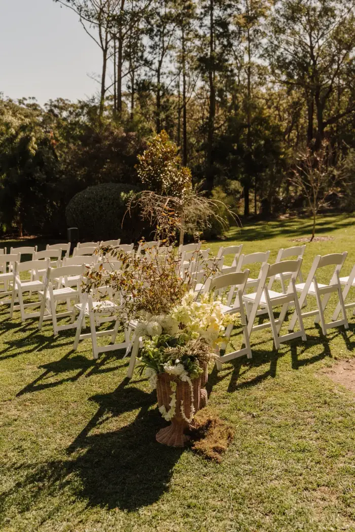 Ceremony aisle with basket flower arrangements between the white chairs