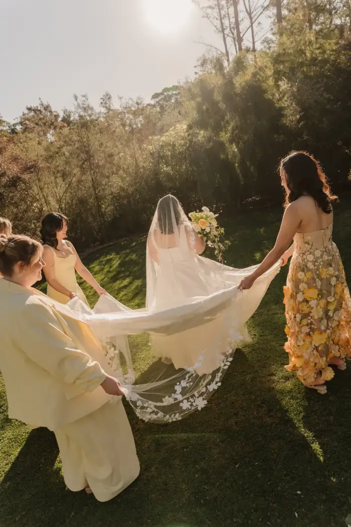 Bridesmaids holding the bride's lace veil out in golden light