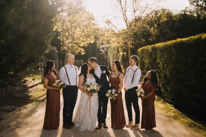 Wedding party portrait with bridesmaids in rust-coloured dresses on a tree-lined driveway