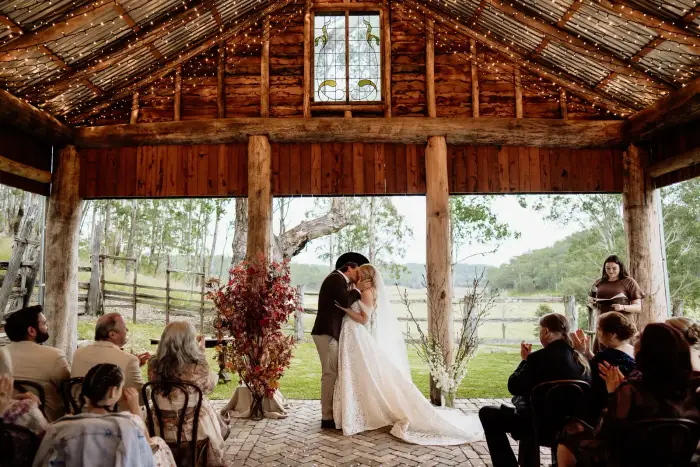 Bride and groom's first kiss under fairy lights in a timber barn ceremony