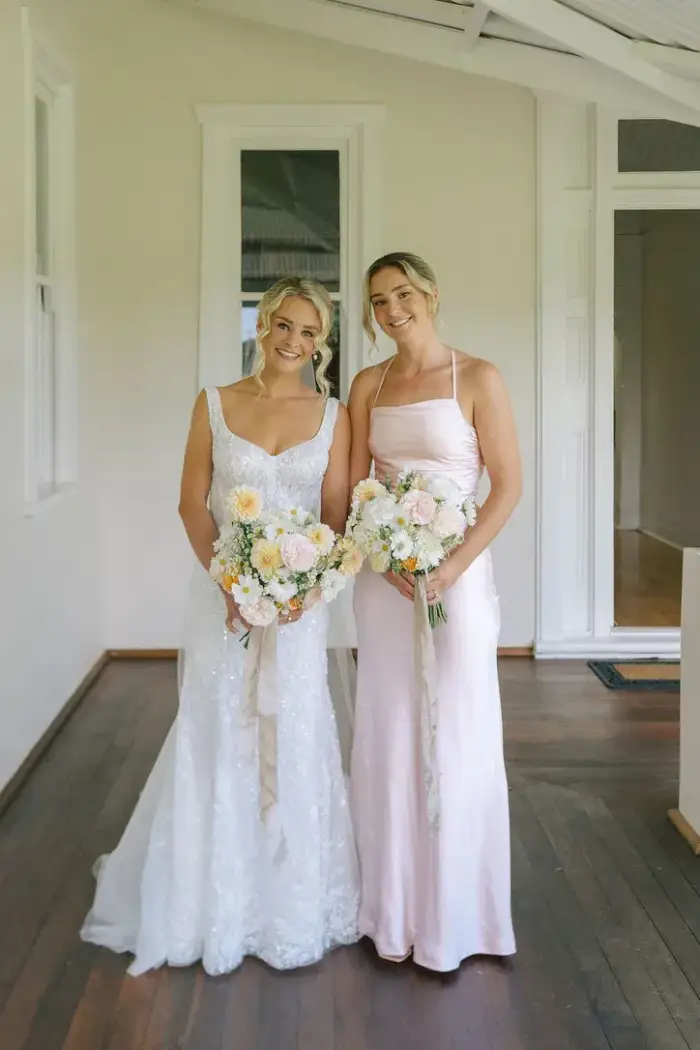 Two bridesmaids in white and blush gowns holding pastel bouquets
