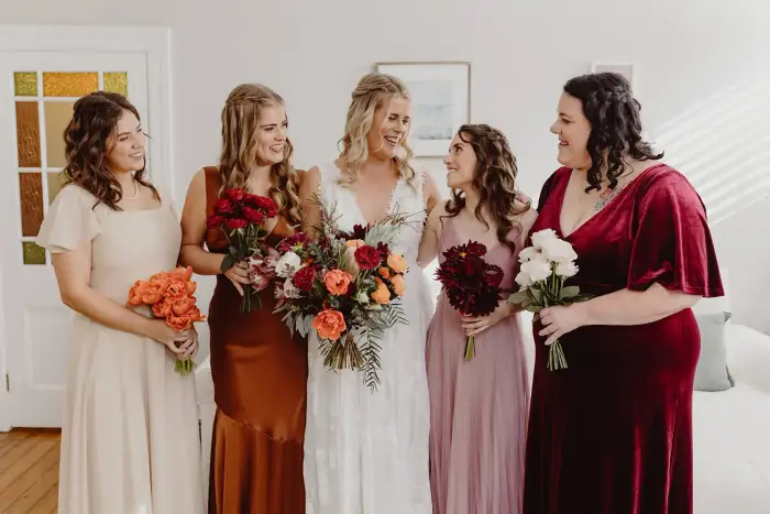 Bridesmaids in mismatched autumn-toned dresses holding burgundy and rust bouquets