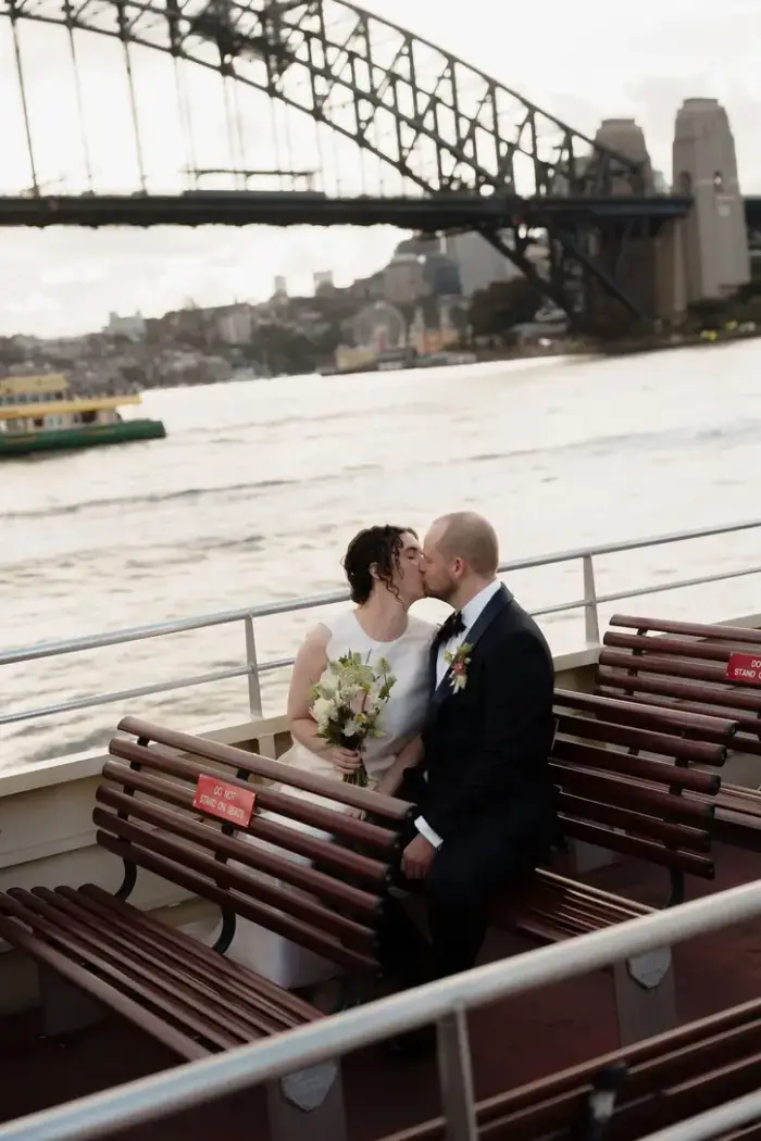 Bride and groom kissing on a ferry with the Sydney Harbour Bridge behind them
